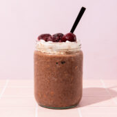 chocolate overnight oats with cream and cherries in jar with spoon