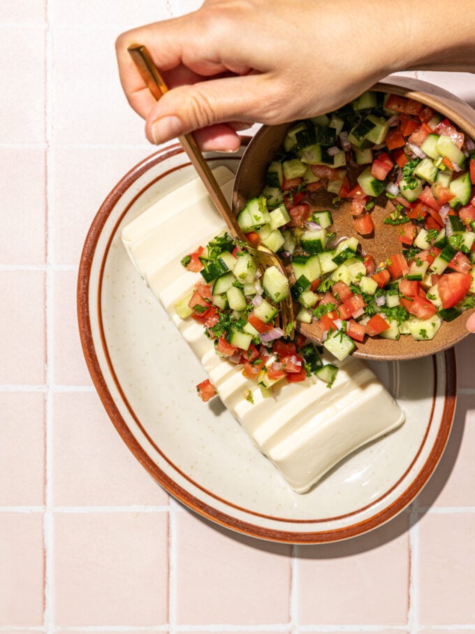 hand pouring salad onto sliced tofu on oblong plate