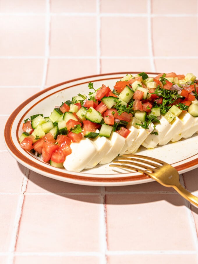 sliced tofu, diced tomato and cucumber on plate with fork on pink tiles