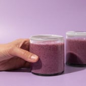 hand holding glass of berry smoothie on purple background